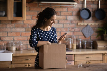 Happy shopper receiving purchase from internet shop, using app on mobile phone for giving positive review to store. Woman packing parcel for sending, using smartphone, ordering delivery service