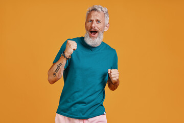 Senior man making a face while standing against orange background