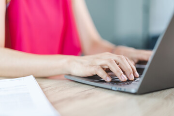 A cheerful middle-aged Asian businesswoman in relaxed casual dress working at home, checking email on computer laptop, writing on financial accounting document paper. Business stock photo
