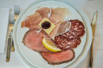 Italian antipasto in a plate at restaurant, with prosciutto, roast beef, soppressa, cheese and jam and a slice of lemon