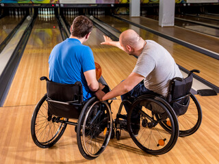 Two young disabled men in wheelchairs playing bowling in the club