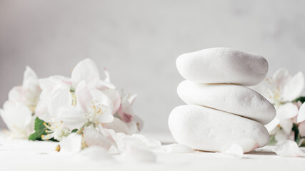 Fototapeta na wymiar Stack of white pebble stones on light plaster surface, with apple flowers. Banner