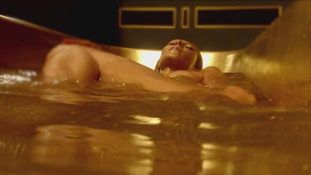 Stylish woman on bikini with shining glitters in her beautiful body swimming and moving inside bathtub . Girl lying in bathroom with golden or yellow color . Close up shot from below under water