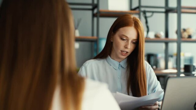 Tracking shot of female applicant during job interview talking to young woman employers. Businesswoman sitting at desk interviewing lady candidate in modern office, close-up. Shooting in slow motion.