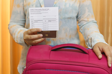 Woman in travel clothes wearing a medical mask showing covid-19 vaccination record card and...