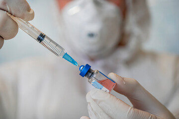 bottle of vaccine close-up in the hand of a doctor with white gloves on a blue background. - obrazy, fototapety, plakaty