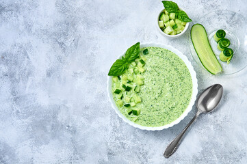Cucumber Gazpacho - cold summer soup with basil in white bowl on light background. Top view Flat lay.