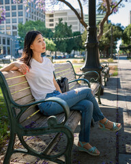 Young Asian Woman Sitting on a Park Bench Under a Jacaranda Tree in Downtown San Jose