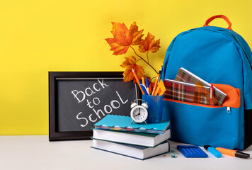 School backpack with colorful school supplies  and blackboard with letters back to school. School supplies on yellow background.