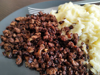 Fried mince beef with mashed potatoes in a black plate.