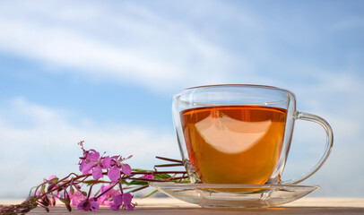 Glass cup of tea with willow-herb on blue sky background