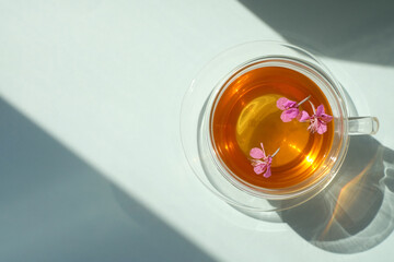 Glass cup of tea with willow-herb, sunlight and shadows, top view, copy space