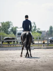 Fotobehang portrait of man rider and black stallion eventing horse trotting leg-yield during equestrian dressage competition in summer © vprotastchik