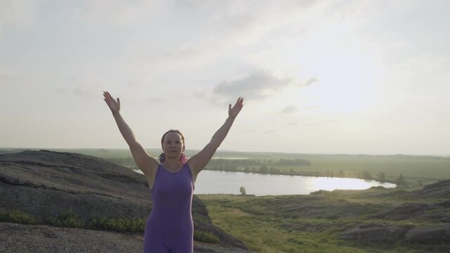 Young woman doing yoga poses, having training session on cliff during sunrise