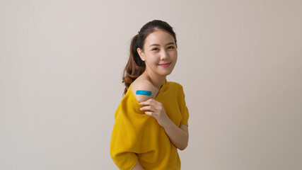 Young attractive beautiful asia female or teenage receive covid-19 anti virus vaccine in campaign vaccination safe life happy smile cheerful with blue, yellow, pink bandage on arm with copy space.