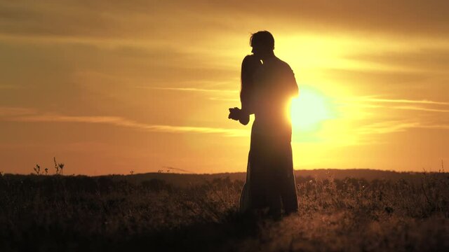 Silhouette of happy young married couple dancing at sunset. Happy man dances and spins with his beloved woman in summer park. Guy and girl are dancing in bright rays of sun in field. Free people.