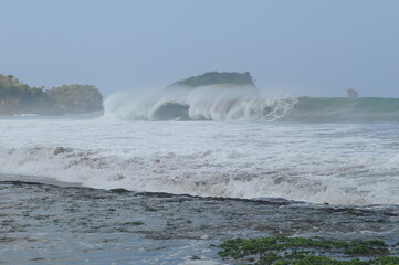 View of sandy beach in Malang district and waves in the sea on a sunny day.