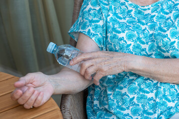 Senior woman hand holds bottle with cold water on her elbow bend. How to stay cool in hot weather.