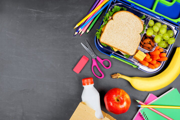 Healthy school lunch box and school supplies. Side border, top view on a chalkboard background.