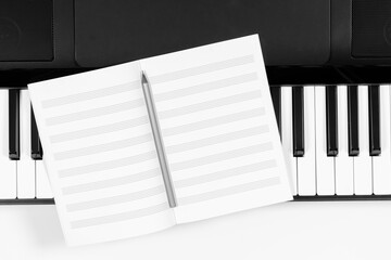 Music learning background. Piano keyboard and open blank sheet music notebook. Top view