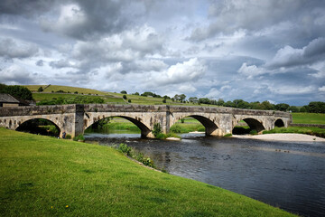 Fototapeta premium Burnsall Bridge over the River Wharfe toward Burnsall and Thorpe Fell, in the Yorkshire Dales, North Yorkshire.