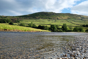 Fototapeta premium A view looking south along the River Wharfe toward Burnsall and Thorpe Fell, in the Yorkshire Dales, North Yorkshire.