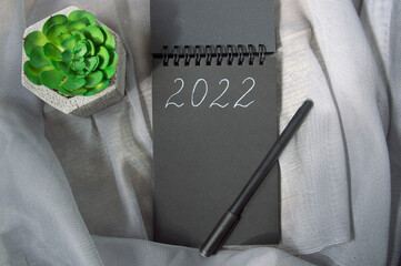 Notebook with an inscription 2022 and into the green plant on gray background.happy new year