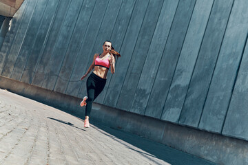 Fototapeta na wymiar Full length of beautiful young woman in sports clothing running outdoors