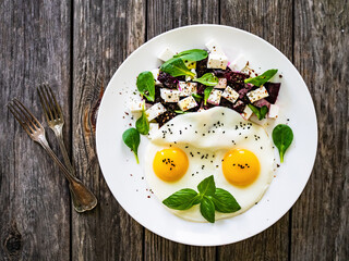 Continental breakfast - sunny side up eggs with beetroots and feta cheese on wooden table

