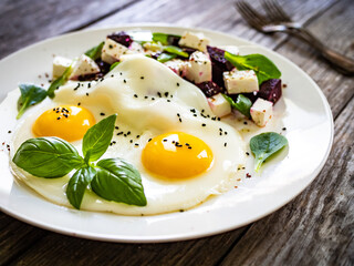 Continental breakfast - sunny side up eggs with beetroots and feta cheese on wooden table
