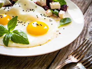 Continental breakfast - sunny side up eggs with beetroots and feta cheese on wooden table
