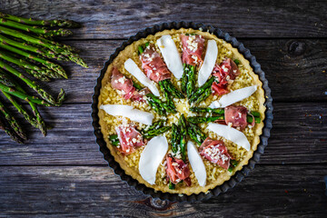 Uncooked tart with asparagus and serrano ham on wooden table
