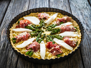 Uncooked tart with asparagus and serrano ham on wooden table
