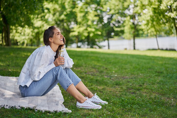 Happy young woman sitting on blanket in city park