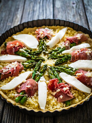 Uncooked tart with asparagus and serrano ham on wooden table
