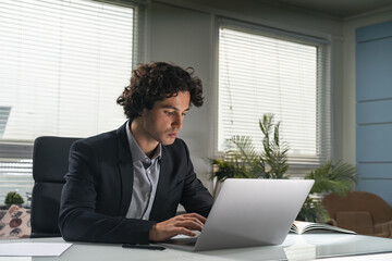 Portrait of thoughtful and concentrated handsome Hispanic businessman in suit sitting at the desk...