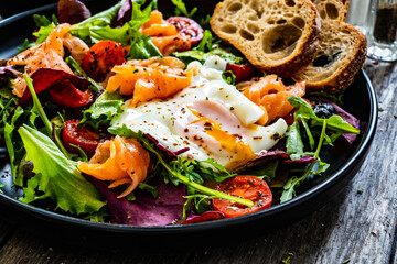 Salmon salad - smoked salmon, sunny side egg and green vegetables on wooden table
