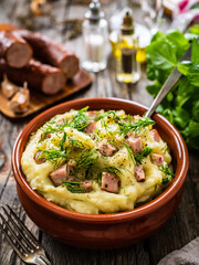 Potato puree - mashed potatoes with sausages and dill in bowl on wooden table