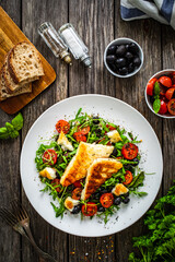 Fresh vegetable salad with grilled halloumi cheese, tomatoes,  lettuce, green leaves, black olives and onion on wooden table
