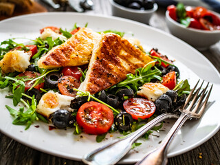 Fresh vegetable salad with grilled halloumi cheese, tomatoes,  lettuce, green leaves, black olives and onion on wooden table
