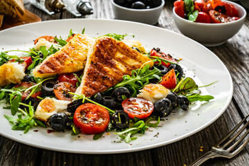 Fresh vegetable salad with grilled halloumi cheese, tomatoes,  lettuce, green leaves, black olives and onion on wooden table
