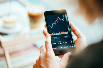 Woman using mobile phone investing application. Stock market investment app in hand. Screen close-up