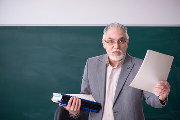 Old male teacher in front of blackboard