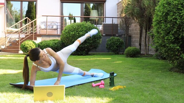 Young fitness woman in sportswear doing side plank exercise outdoors.