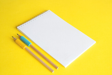 Blank notebook and two pencils on yellow background