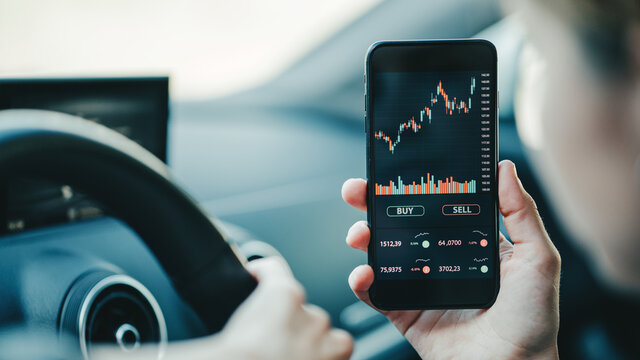 Woman using mobile phone investing application in car. Stock market investment app in hand. Close-up view