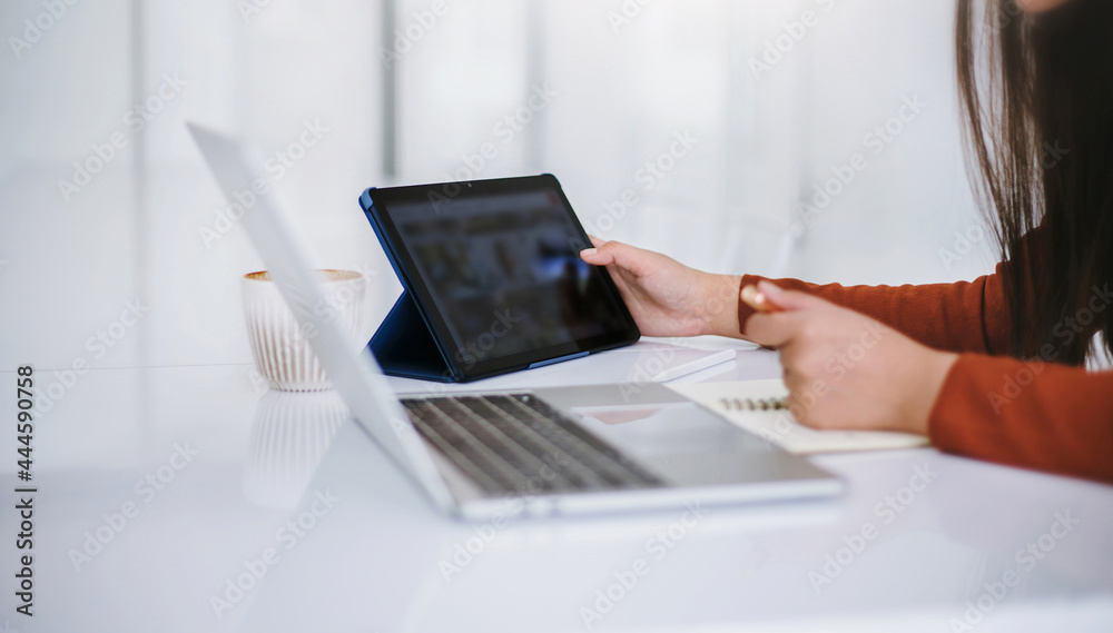 Wall mural Focus on hand young asian woman holding pen and open notebook while she working at home with computer laptop