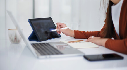 Focus on hand young asian woman holding stylus pen pointing on digital tablet while she working at home with computer laptop