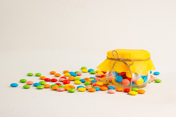 Chocolate candies, small multi-colored in a jar with a bow, on a gray background and with a yellow lid.