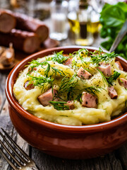 Potato puree - mashed potatoes with sausages and dill in bowl on wooden table